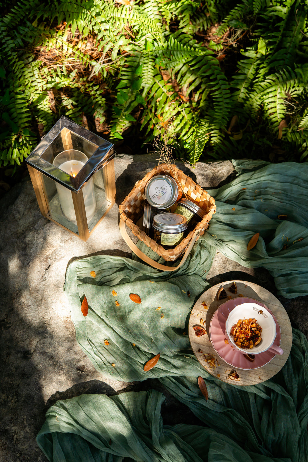 Baskets with jars of preserves and a candle lantern on a green fabric background.