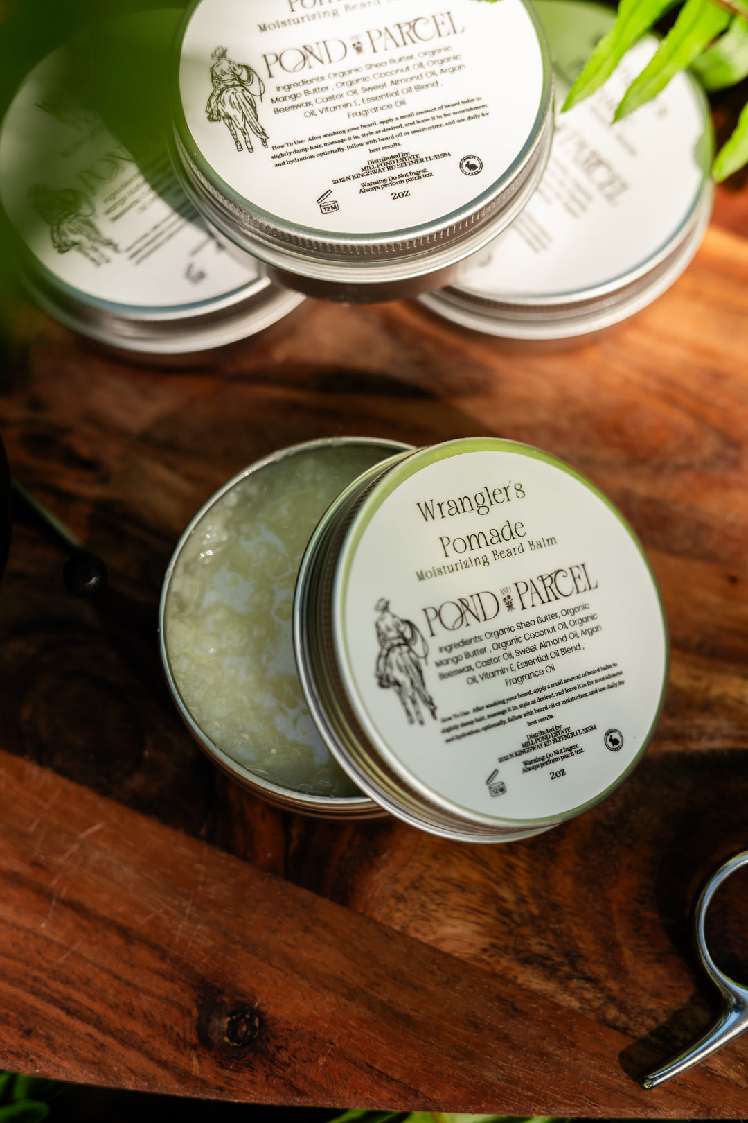 Wranglers Pomade Moisturizing Balm in round metal tins, with one tin open to show the balm inside.