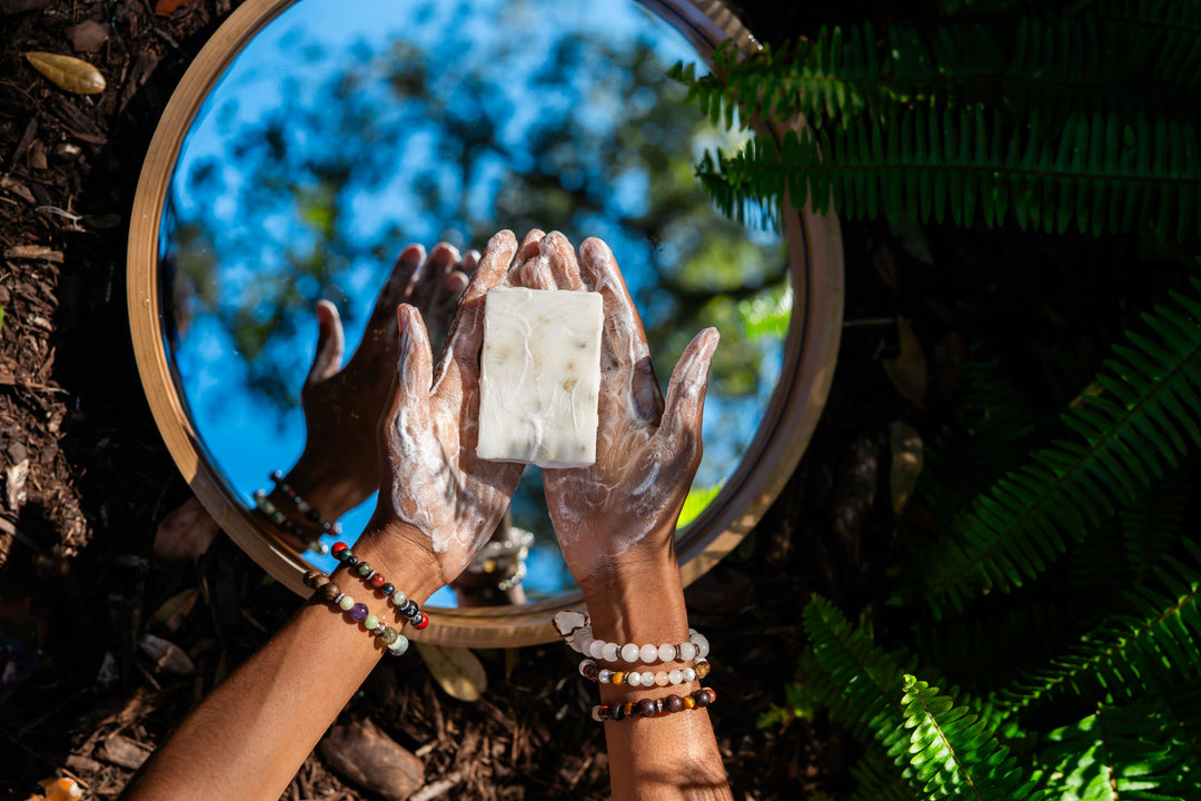 Hands holding a crystal in front of a mirror with a natural background