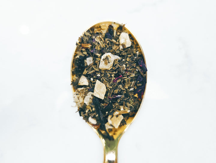 Gold spoon filled with a mix of dried herbs.